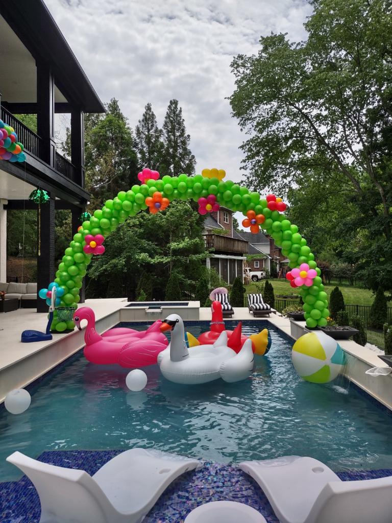 green balloon arch with flowers over swimming pool