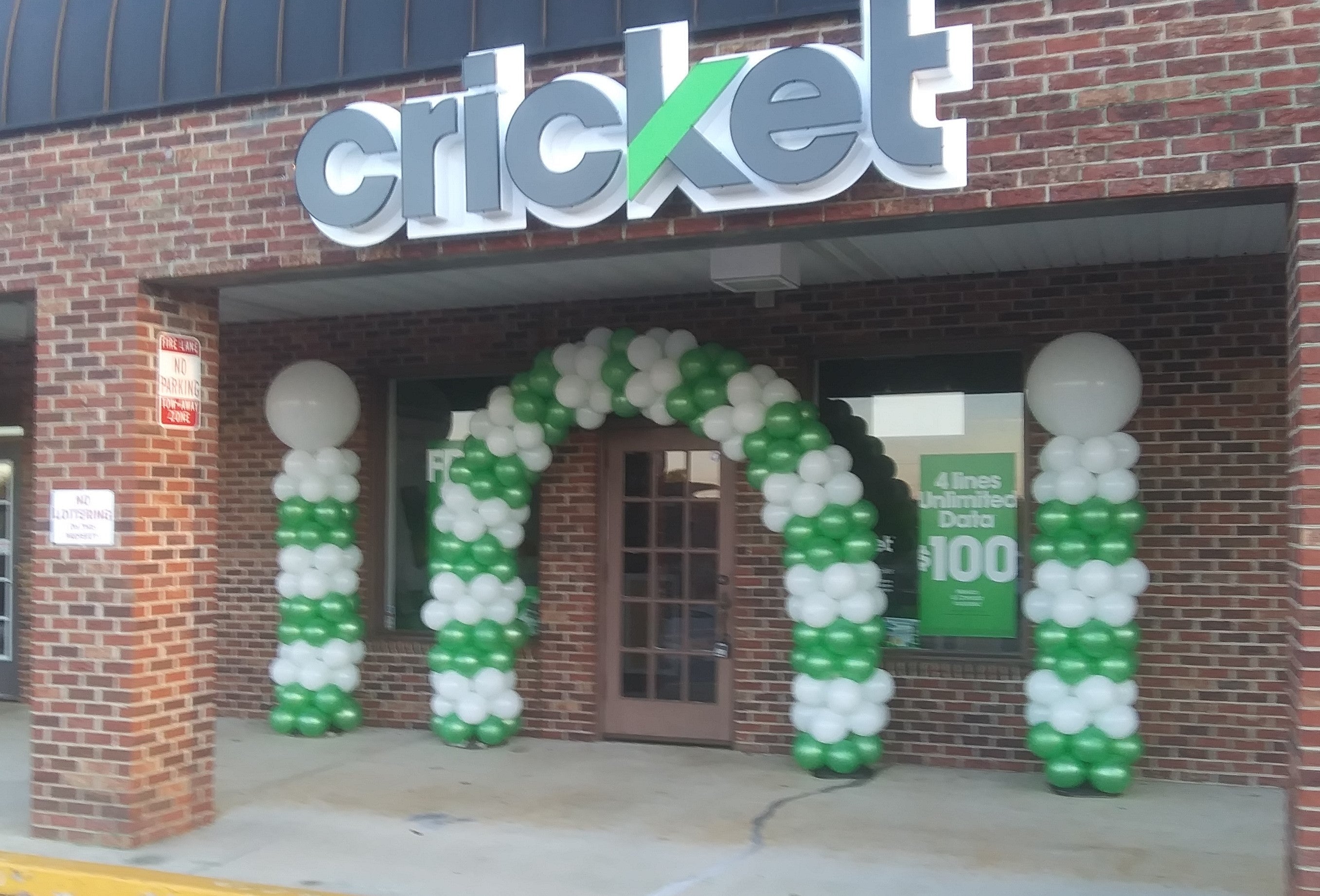 balloon arch and columns, green and white with big white balloons on top setting in front of a cricket mobile store.
