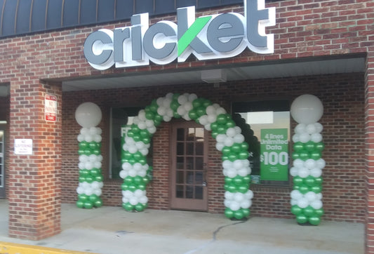 balloon arch and columns, green and white with big white balloons on top setting in front of a cricket mobile store.