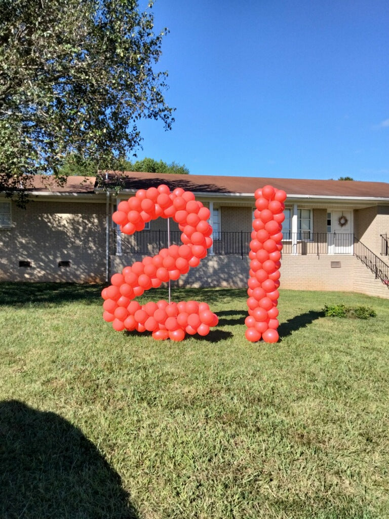 A set  of large sculpted balloon numbers made in red balloons a 2 and 1 installed in a yard on a lawn in front of a house.