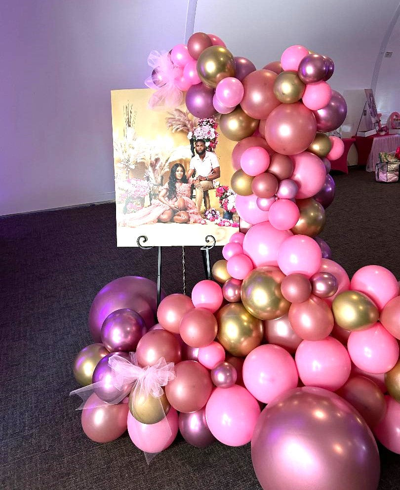 Shades of pink balloon garland with gold chrome balloons on easel with pink bow with baby shower picture