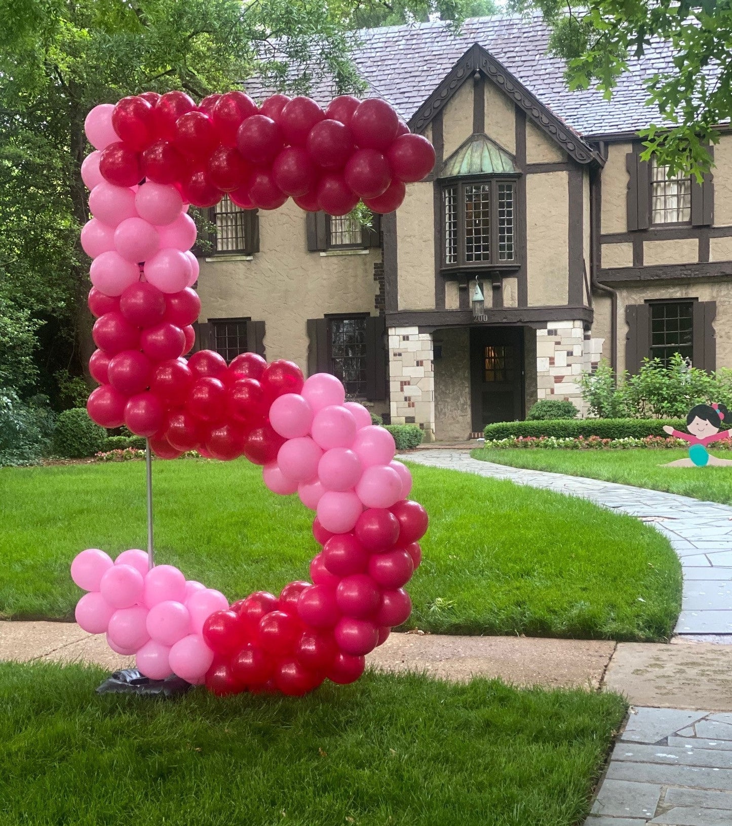 large balloon sculpture  number 5 made with pink and red balloons on a lawn in front of a house.