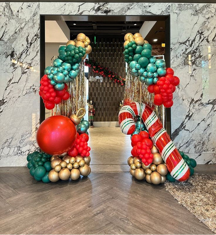 Decorative Christmas balloon arches in red, green, and gold at the entrance of a building.