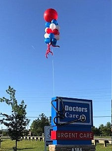balloon column with big balloon on top floating high in the sky over a sign