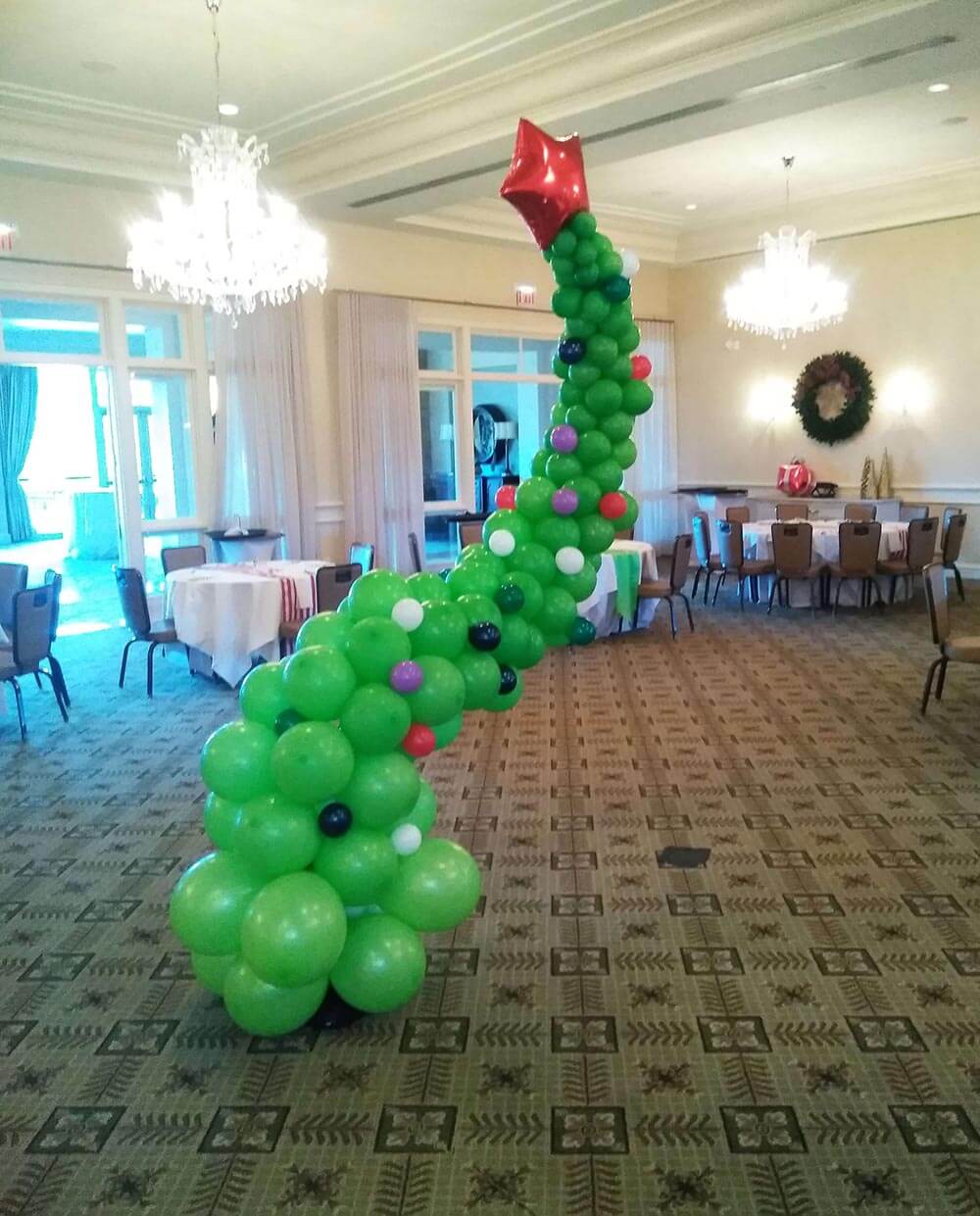 Grinch Balloon Christmas Tree with red star on top.  decorated green curved tree in a ballroom