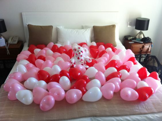 Bed covered with red, white and pink Heart Balloons with red and white bear in the center.