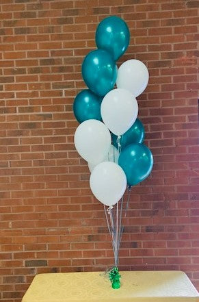 a balloon centerpiece of 10 helium party balloons in a bouquet tied with ribbon on a green weight on a table top.