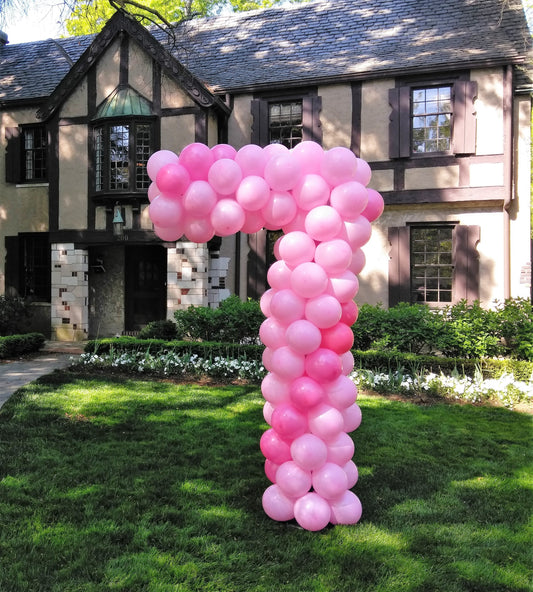 large balloon sculpture number 7 made with pink balloons on a lawn in front of a house.